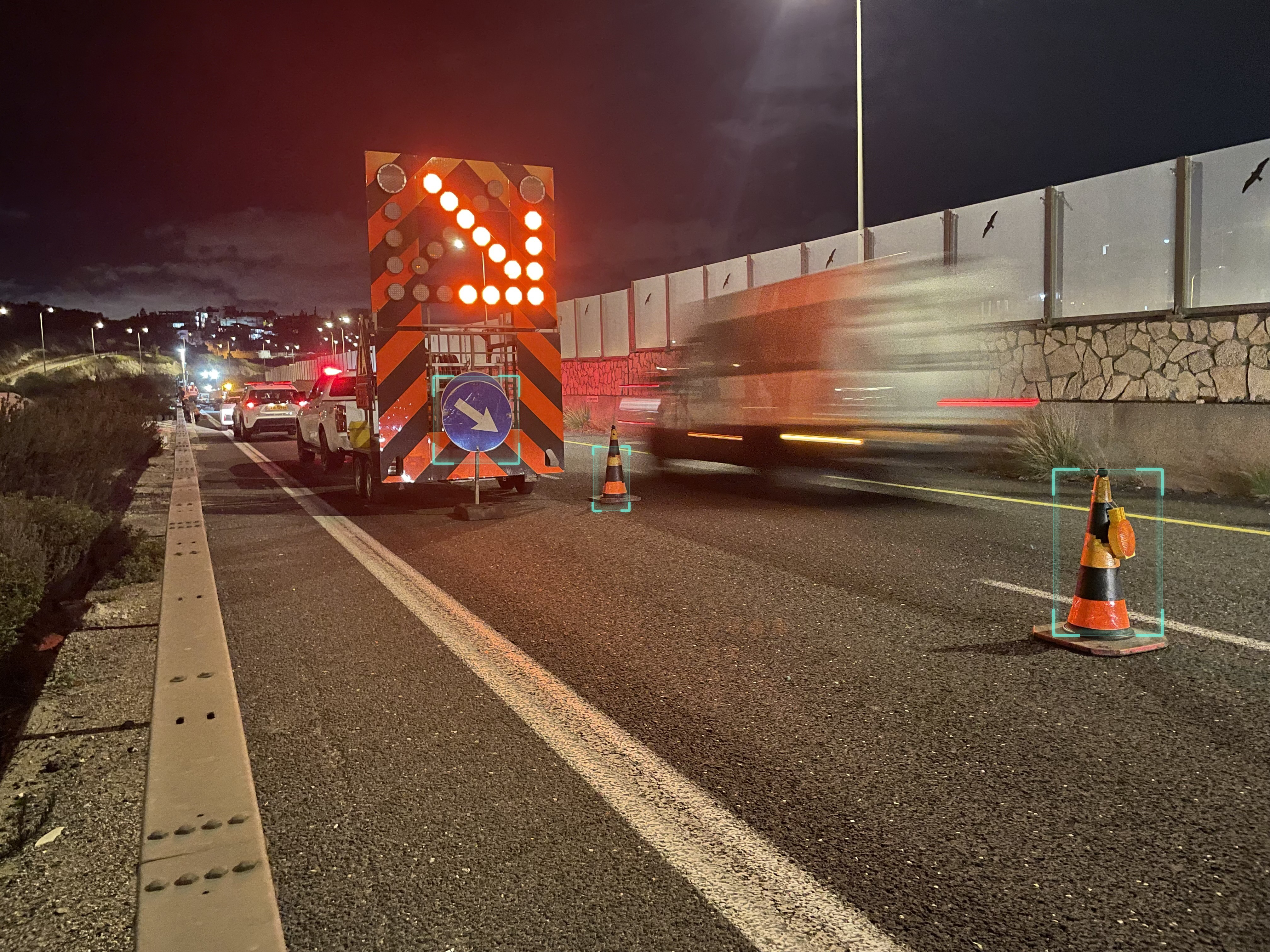 Night roadworks with an illuminated directional arrow and traffic cones highlighted by visual detection markers